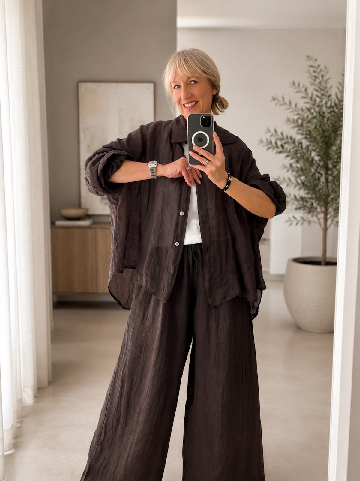 Ganzkörperansicht der schokobraunen Bluse Aria aus Leinen im edlen Set-Look mit passender weiter Leinenhose an einem Modell im modernen Loft-Studio