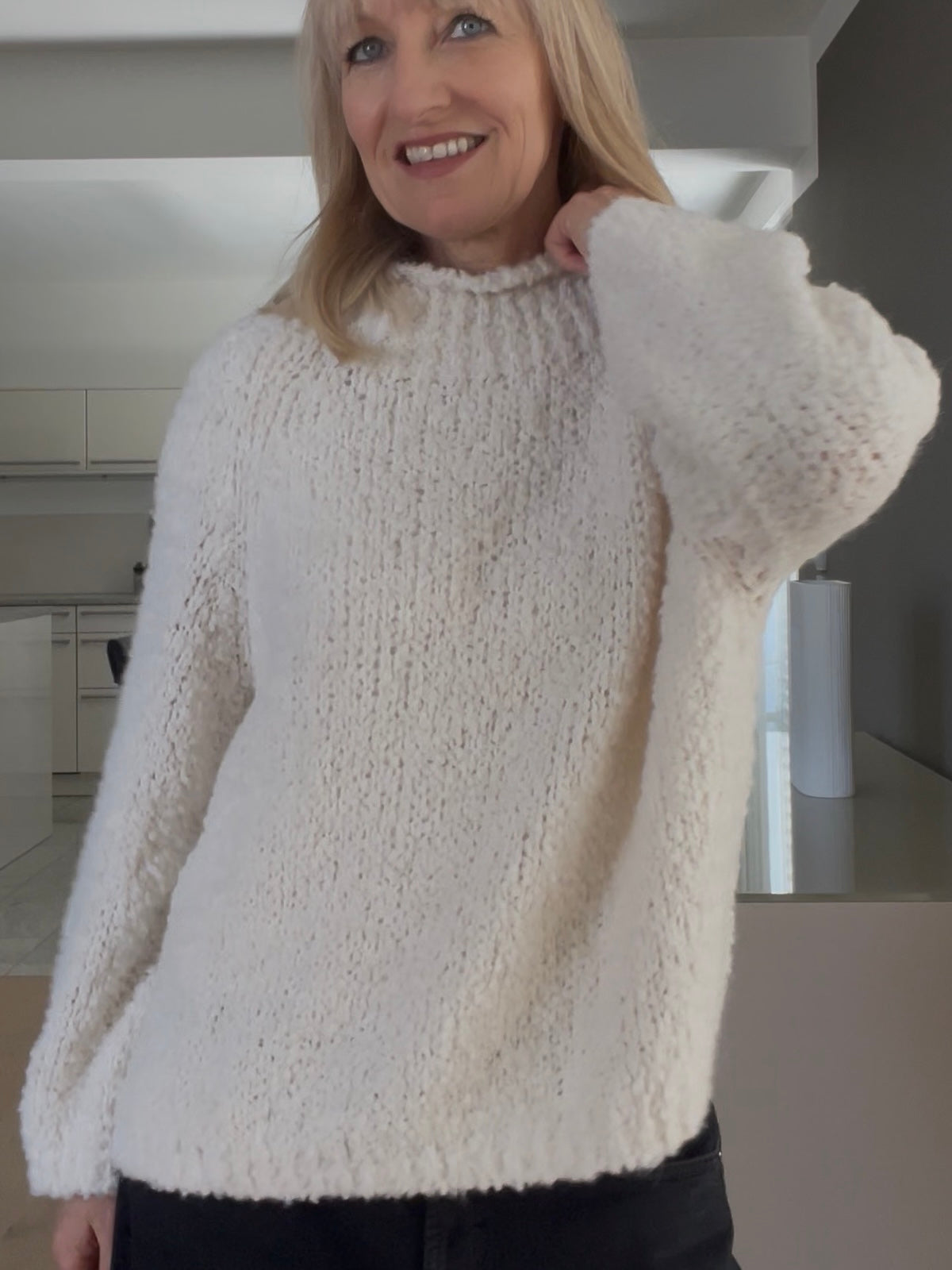 Eine modebewusste Frau trägt den edlen Pullover Jola in Creme, gestylt mit hohem Halsausschnitt und prägnanter Formsprache, kombiniert mit dunkler Denim.