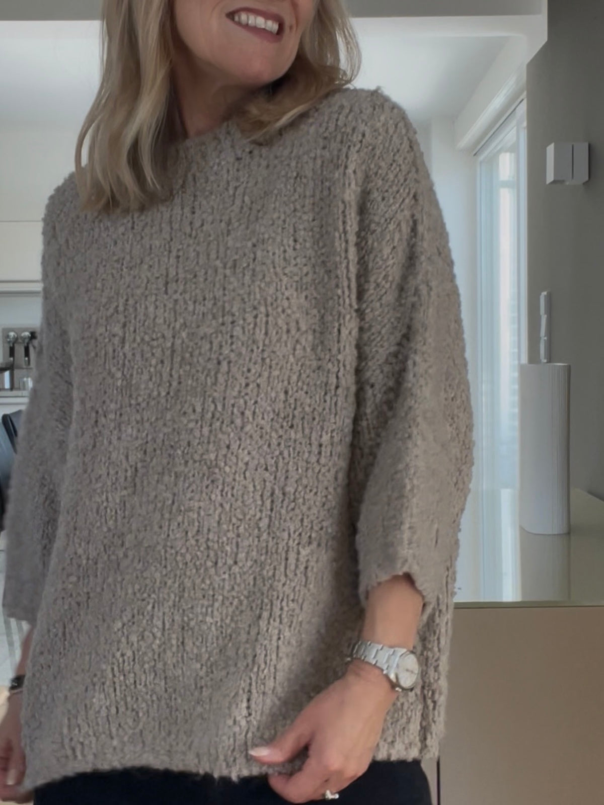 Eine modebewusste Frau trägt den edlen Pullover Jola in Greige, gestylt mit hohem Halsausschnitt und prägnanter Formsprache, kombiniert mit dunkler Denim
