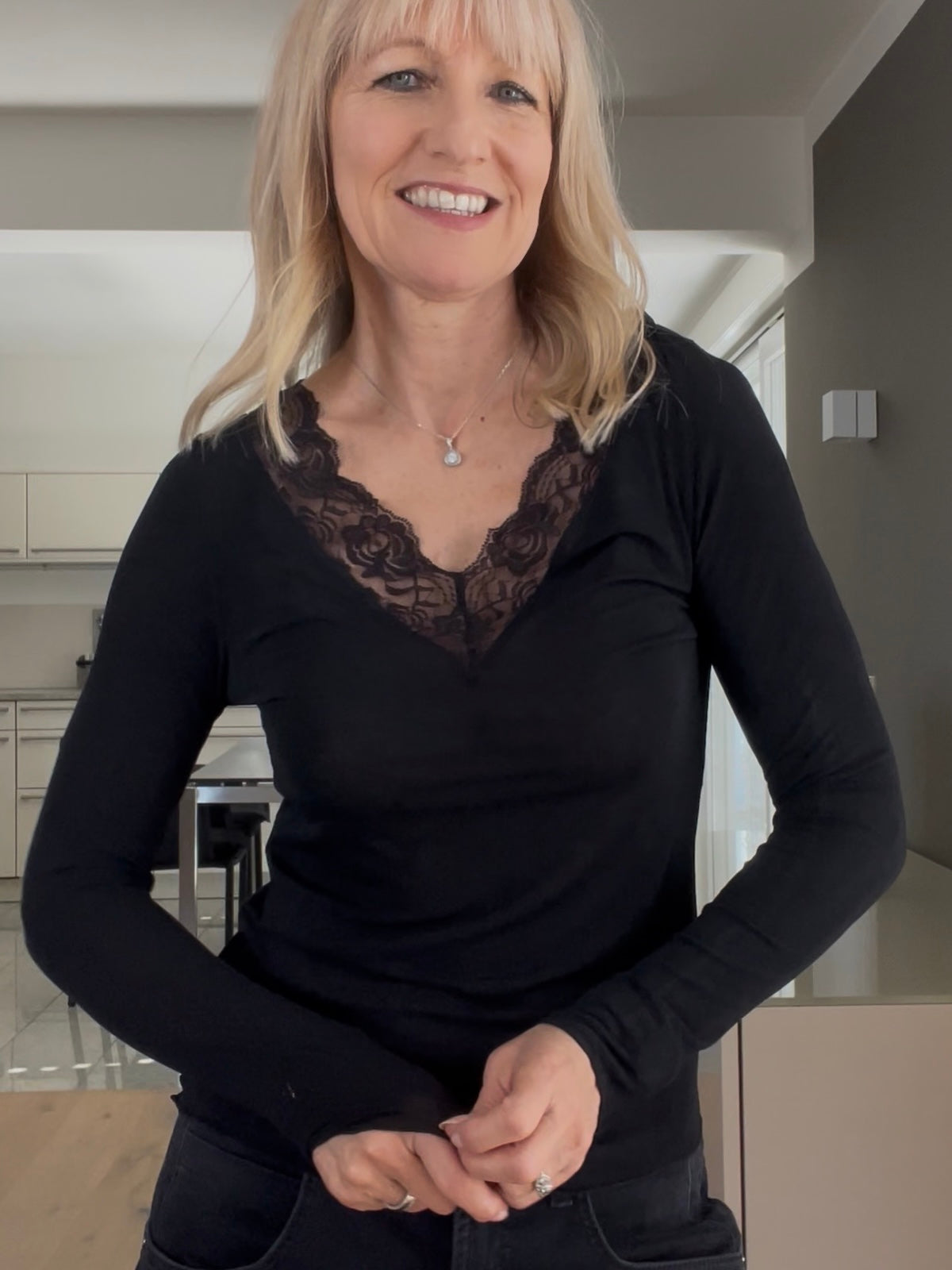Eine modebewusste Frau trägt das edle Shirt Luna in Schwarz, perfekt gestylt mit tiefem V-Ausschnitt und femininem Spitzenbesatz zur dunklen Denim.