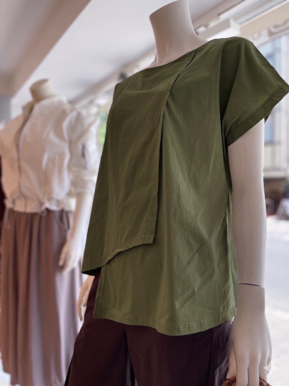 Clean geschnittenes Damen Shirt Marta in Grün mit geometrischem Layer-Look auf einer Schaufensterpuppe dekoriert im exklusiven Store-Ambiente