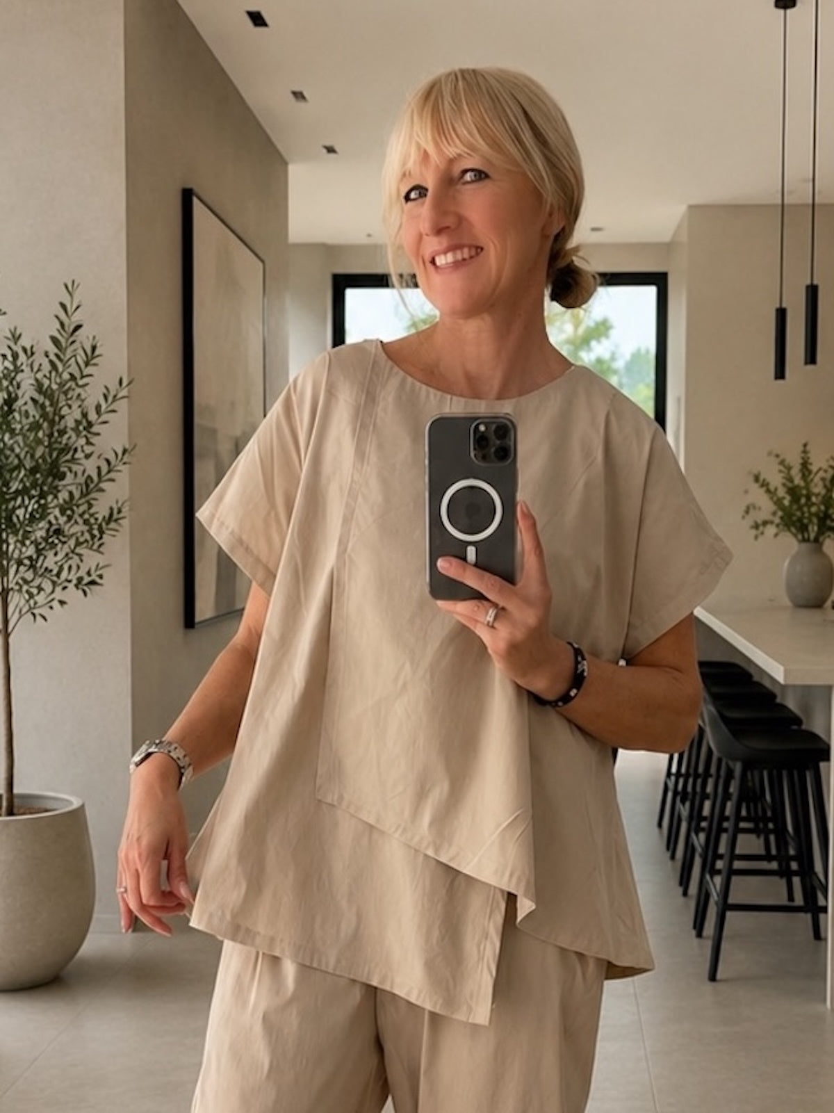Frontale Nahaufnahme des asymmetrischen Shirts Marta in Stone an einem blonden Modell zur optimalen Veranschaulichung des modernen, strukturierten Boxy-Styles, der überschnittenen Schulterpartie und der edlen, klar definierten Linienführung.