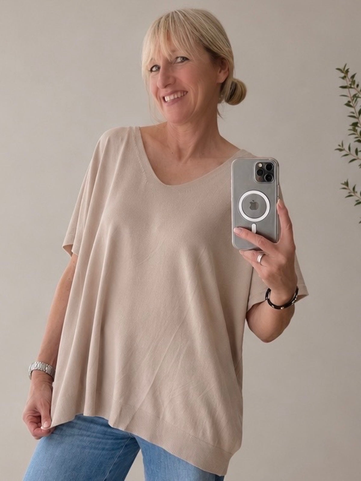 Blondes Modell (1,68 m) trägt im Spiegel-Selfie das weit fallende, beige V-Neck Shirt Maria. Der fließende Stoff umspielt locker die Figur, lässig kombiniert mit einer weiten Blue Jeans.