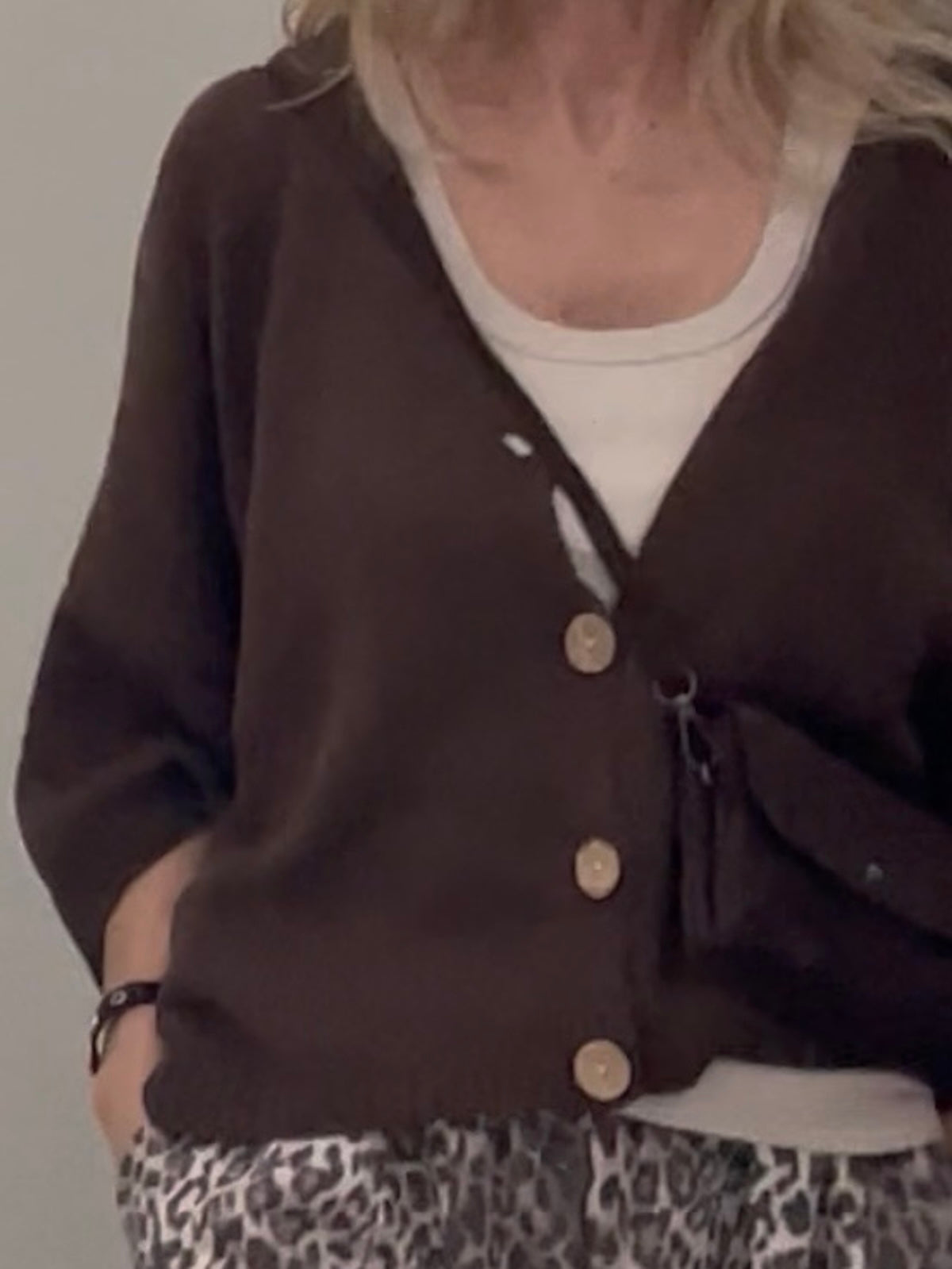 Eine blonde Frau trägt den braunen Strick Cardigan Daisy mit V-Ausschnitt und hellen Knöpfen zur gemusterten Hose. SILKE MODEN Kitzingen.