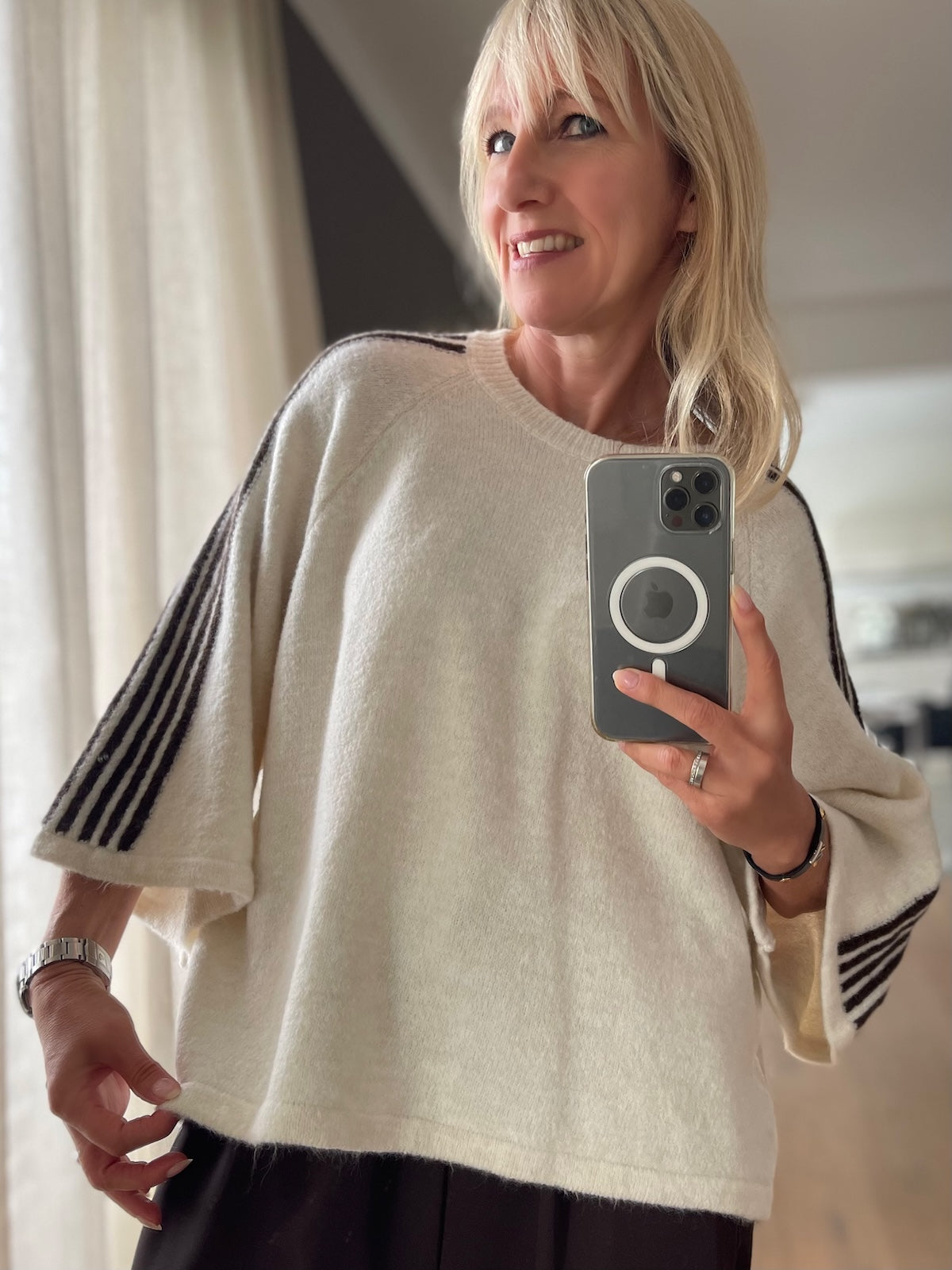 Modebewusste Frau trägt den cremefarbenen Strick-Pullover Ameli mit sportiven dunklen Kontraststreifen an den weiten 3/4-Ärmeln im modernen Boxy-Schnitt.