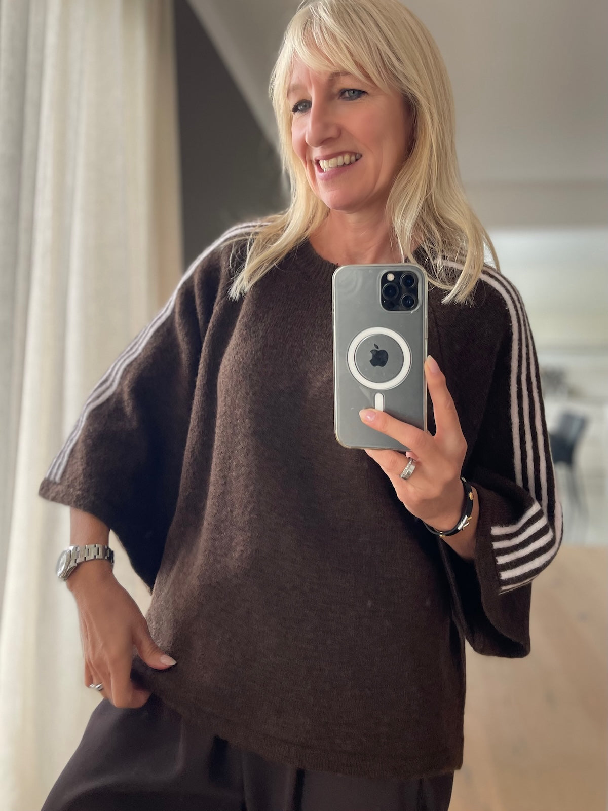 Modebewusste Frau trägt den schokobraunen Strick-Pullover Ameli mit sportiven weißen Kontraststreifen an den weiten 3/4-Ärmeln im modernen Boxy-Schnitt.