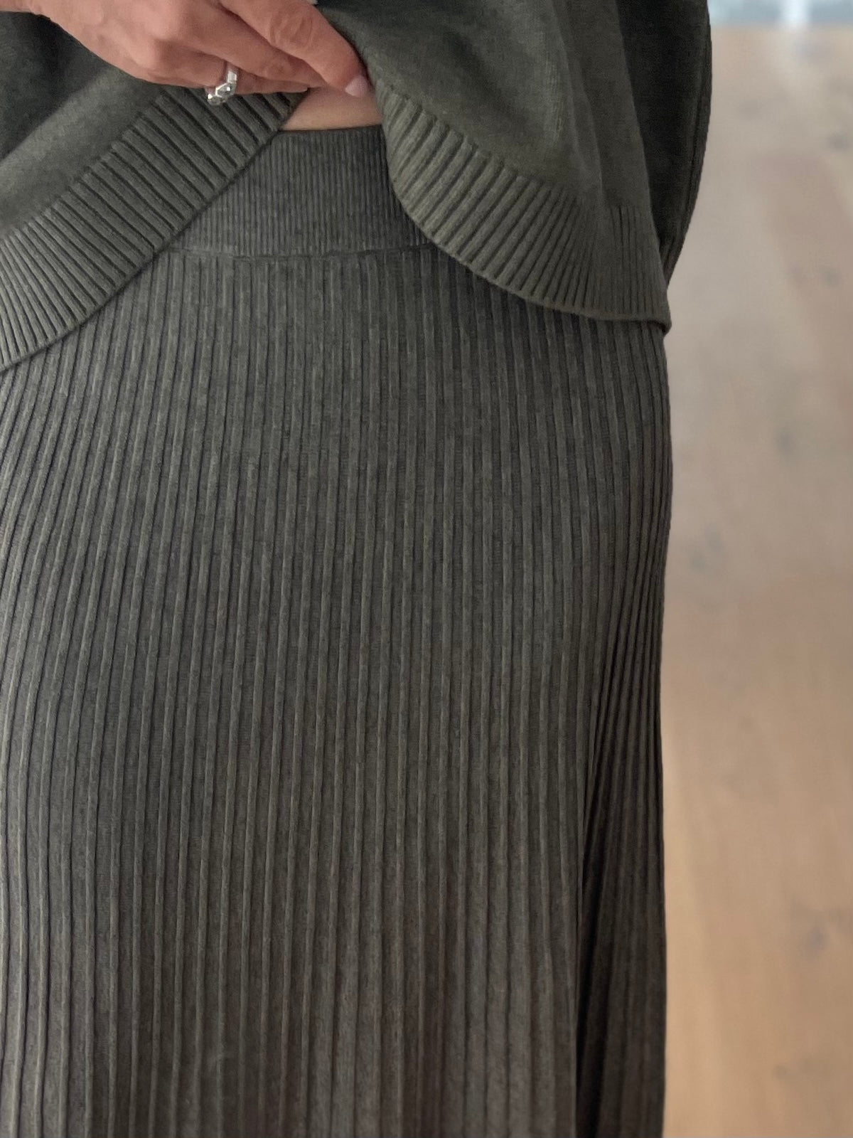 Nahaufnahme des grünen Strickrocks Elise, die die edle Plissee-Struktur, das kompakte Maschenbild und den festen Elastikbund am Bauch zeigt.