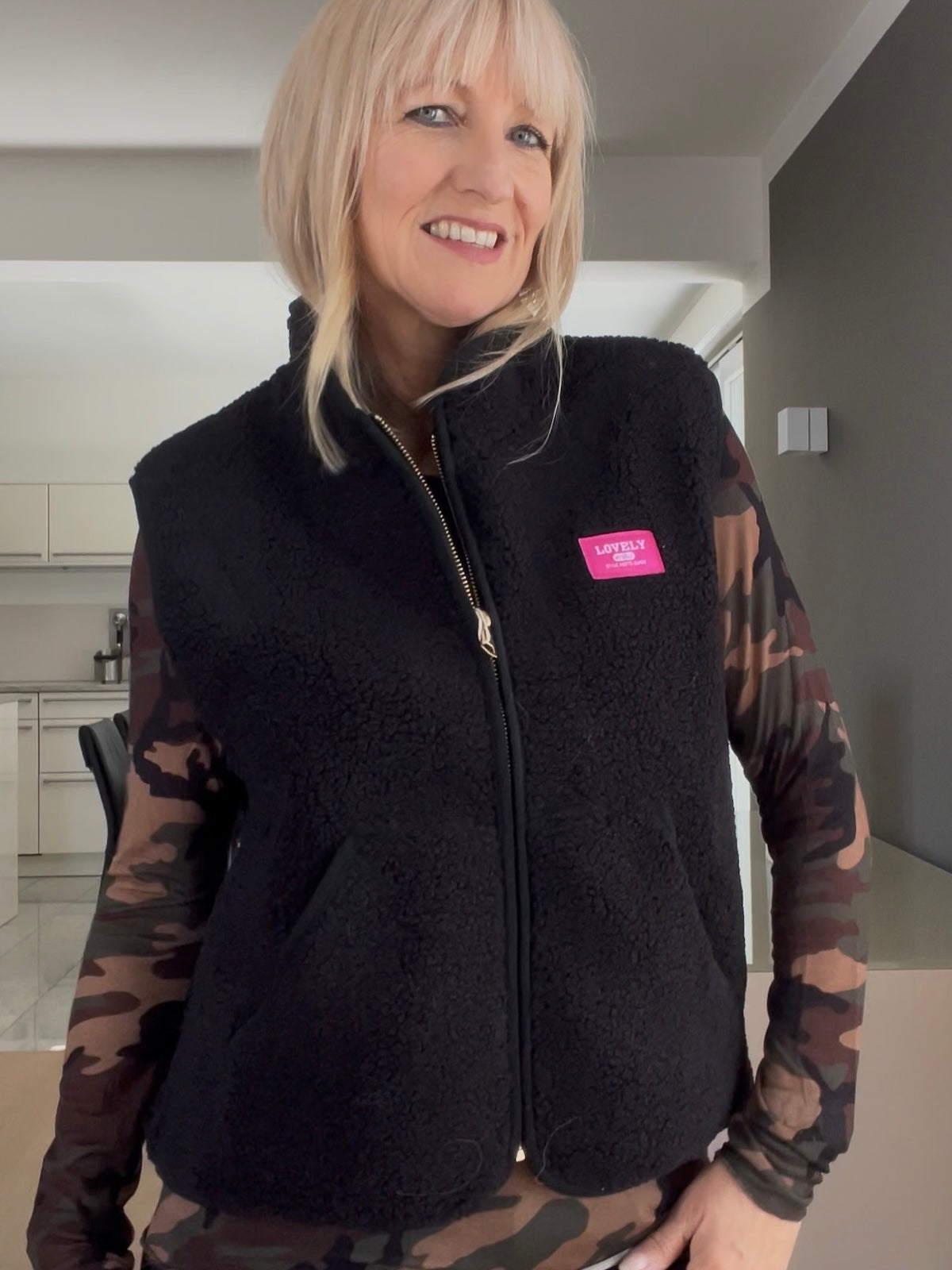 Nahaufnahme der schwarzen Weste Kira, welche den strukturierten Fall, den edlen Reißverschluss in Goldoptik und die seitlichen Eingrifftaschen im Layering-Look zeigt.   