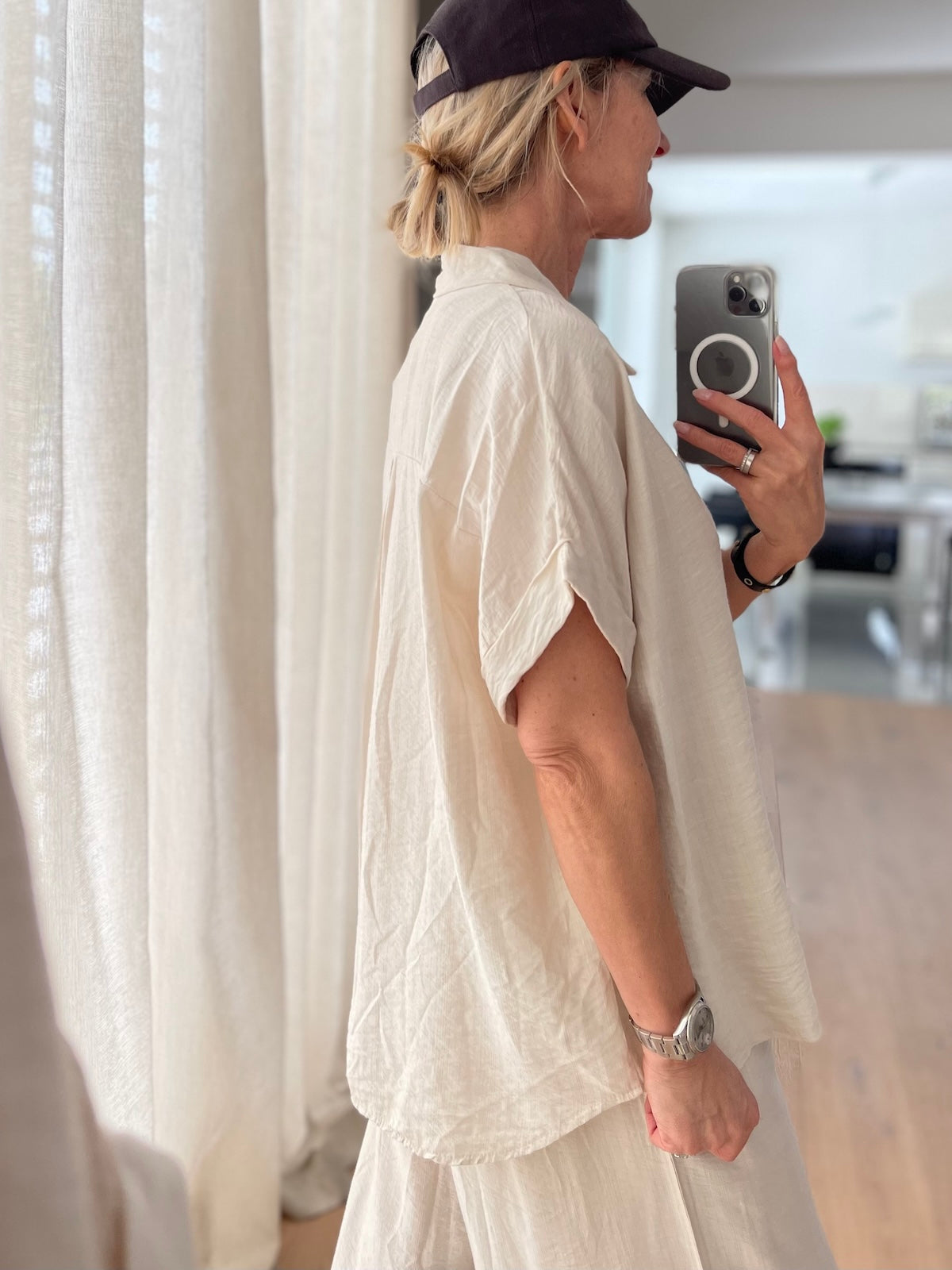 Seitenansicht des hellbeigen Zweiteilers Chloe im Spiegel-Selfie. Das lockere Oberteil mit überschnittenen Ärmeln fällt lässig und fließend über die weite Stoffhose.